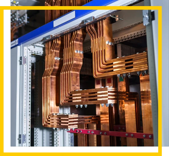 Close-up of multiple copper busbars arranged in parallel inside an industrial electrical panel, showing detailed bends, bolts, and connections. The panel is framed by a yellow and white border.