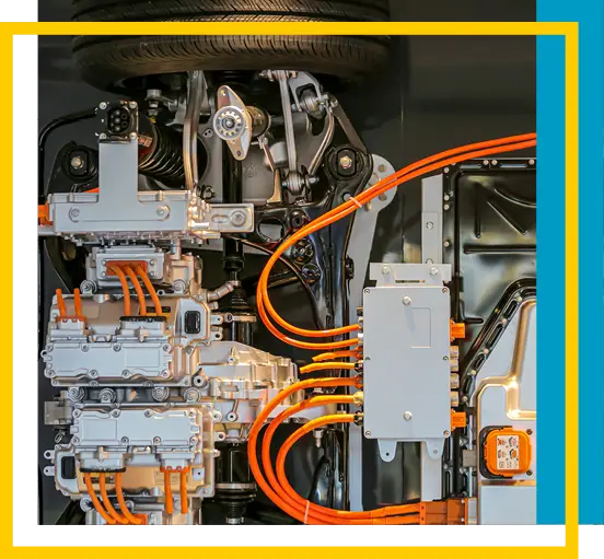 Close-up view of an electric vehicles motor and battery system, showing interconnected orange cables, metallic components, and a partially visible tire at the top, framed by yellow, white, and blue borders.