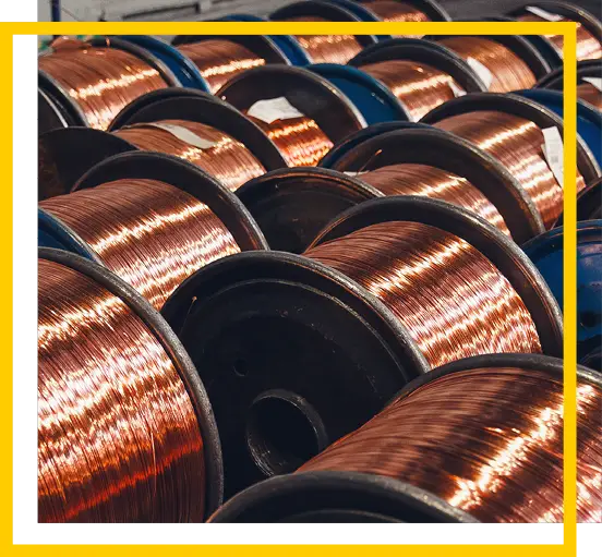 Large spools of shiny copper wire are lined up in rows inside an industrial setting, reflecting light. A yellow and white border frames the image.