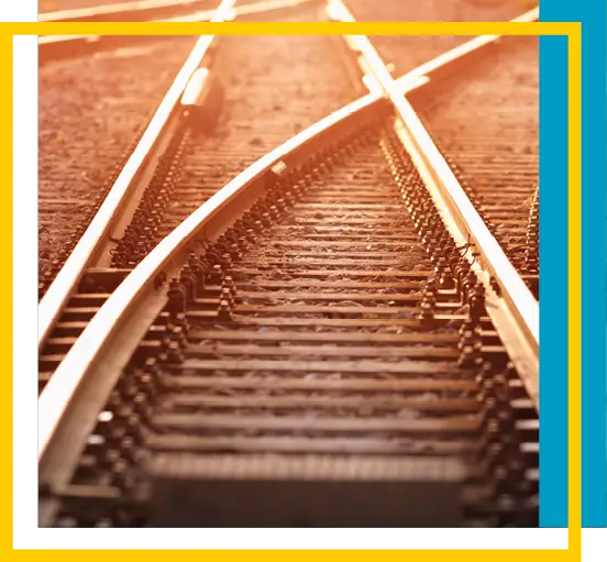 Railway tracks splitting into two directions with sunlight shining on the rails. The image is framed by white, yellow, and blue borders.